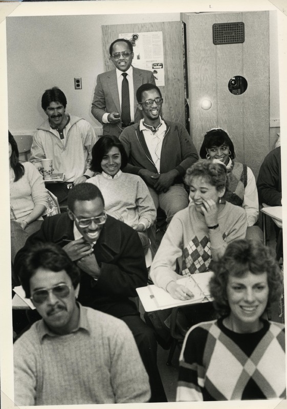 Smiling students seated in classroom with professor in back